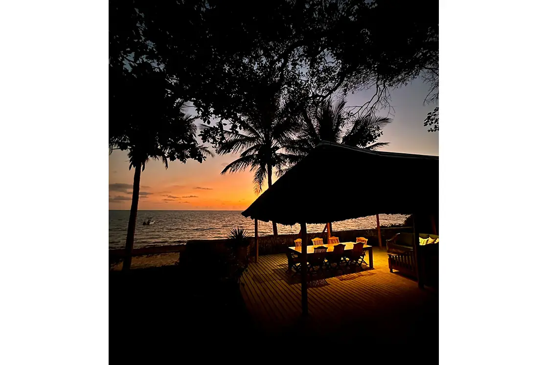 Perfect Hideaways real estate property: A gazebo-covered dining table with soft orange lighting, featuring a sunset view and surrounding vegetation. Villa 1b Beach House, Vilanculos.