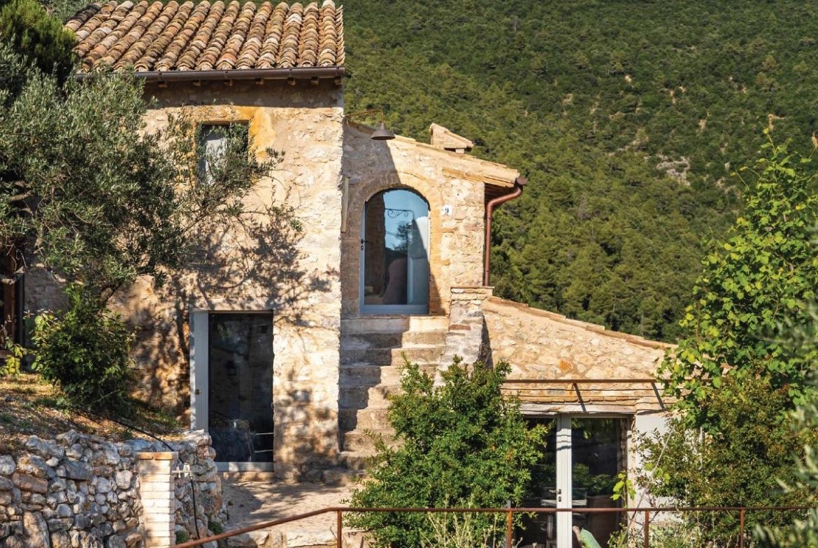 Perfect Hideaways real estate property: Natural stone villa with terracotta roof tiles and modern glass doorways showcasing Tuscan architectural elements. Casa Di Led in Spoleto.