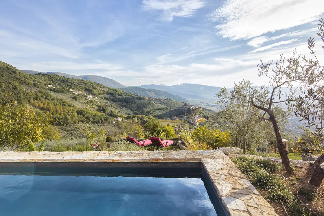 Perfect Hideaways real estate property: A view of the Italian countryside from a sparkling swimming pool. Clear sky and blue water give way to rolling hills. Casa Di Led in Spoleto.