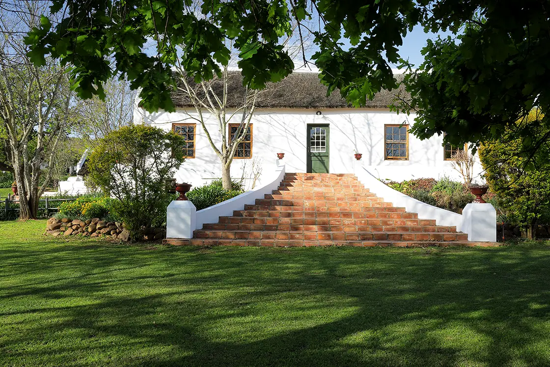 Perfect Hideaways real estate property: Outdoor steps leading to thatch-roofed Cape-Dutch farmhouse. Central green door and symmetrical window placement. Zeekoegat Farm in Riversdale.