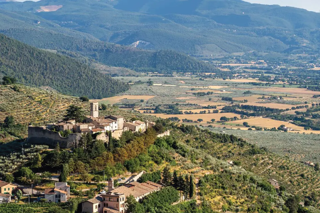 Perfect Hideaways real estate property: A landscape photo of the restored 17th-century stone villa established on a hilltop in Umbria, with views of the farmland and mountains in the background. Casa Di Led in Spoleto.