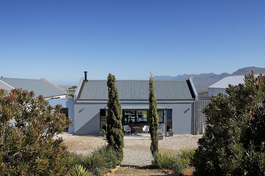 Perfect Hideaways real estate property: A house featuring a corrugated roof and a paved driveway, set against a clear sky backdrop. HaesFarm in Stanford.