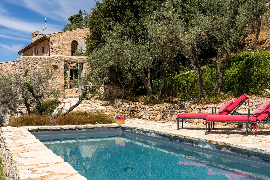 Perfect Hideaways real estate property: A natural stone walkway beside a sparkling swimming pool, which leads to the stunning courtyard. Sun loungers next to clear blue water. Casa Di Led in Spoleto.