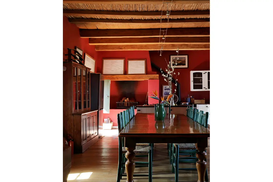 Perfect Hideaways real estate property: Dining room within the main house featuring red walls, wooden floors, and dining table surrounded by blue chairs. Zeekoegat Farm in Riversdale.