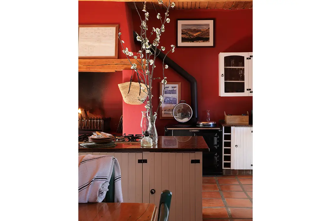 Perfect Hideaways real estate property: Central kitchen island featuring black stone countertop, with built-in gas stove top. Against the back wall is an additional stove and indoor fireplace. Zeekoegat Farm in Riversdale.