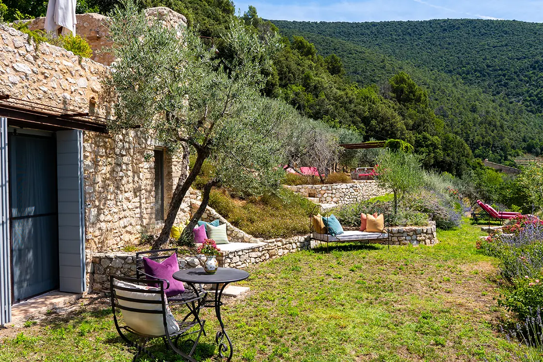 Perfect Hideaways real estate property: An outdoor garden with numerous comfortable seating areas, on the left of the garden is a natural stone guest room with blue shuttered doors. Casa Di Led in Spoleto.