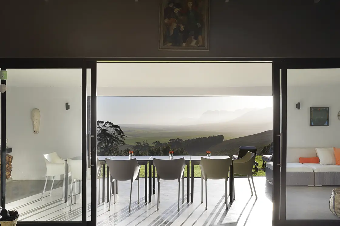 Perfect Hideaways real estate property: A view from inside a house showcasing the exterior landscape through a window and an outdoor dining area. HaesFarm in Stanford.