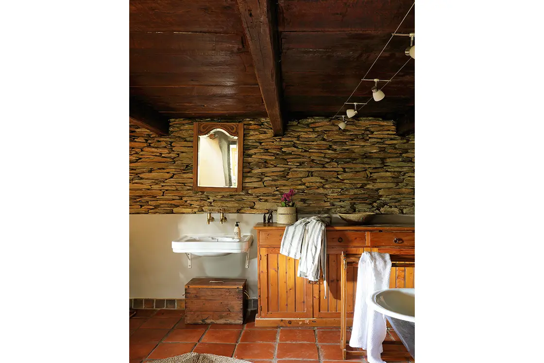 Perfect Hideaways real estate property: Heritage-style bathroom featuring raw stone walls and dark ceilings. Basin, free-standing bath, and wooden cupboard. Zeekoegat Farm in Riversdale.