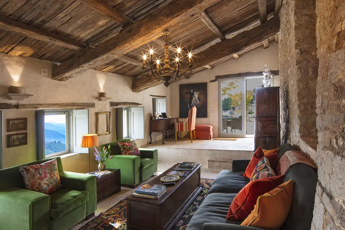 Perfect Hideaways real estate property: A spacious living area, featuring a grand chandelier. Natural stone and limewash interior walls support a sloping wood ceiling. Casa Di Led in Spoleto.