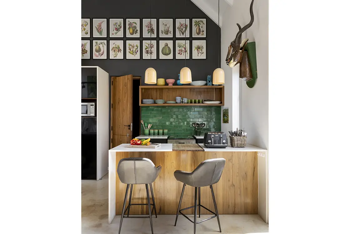 Perfect Hideaways real estate property: A contemporary kitchen with bar seating, overhead lighting, and a green tiled backsplash above the stove. Grey walls decorated with vintage botanical prints. Barncroft in Napier.