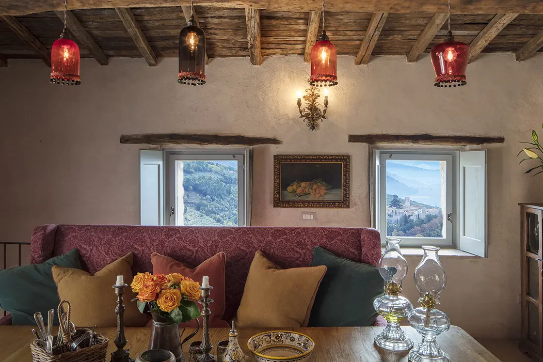 Perfect Hideaways real estate property: Pink paisley couch with muted decorative pillows, and complementary pink glass lighting above a rustic table arrangement. Casa Di Led in Spoleto.