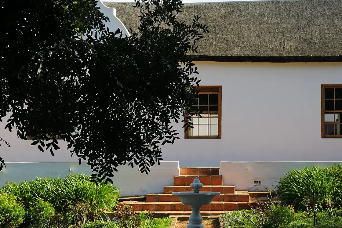 Perfect Hideaways real estate property: Garden courtyard water feature surrounded by symmetric footpaths, a nearby Cape-Dutch style homestead with connected patio steps. Zeekoegat Farm in Riversdale.