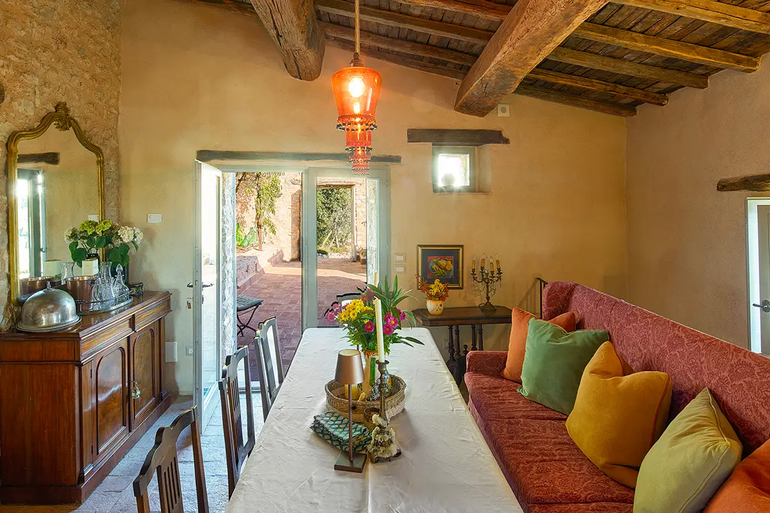 Perfect Hideaways real estate property: A dining room, featuring a comfortable pink couch with muted cushions, the room has a natural stone interior, limewash walls, and an aged-wood ceiling. Casa Di Led in Spoleto.