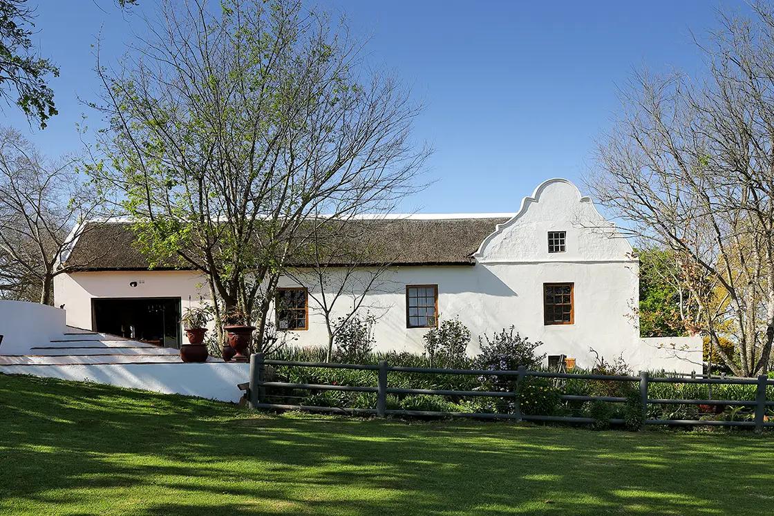 Perfect Hideaways real estate property: A Cape-Dutch style farmhouse with a manicured lawn, and veranda steps leading to the outdoor fireplace area. Zeekoegat Farm in Riversdale.