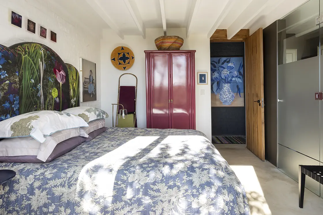 Perfect Hideaways real estate property: A bedroom with a double bed and an en-suite bathroom. Blue and purple tones complement a white brick wall. Barncroft in Napier.