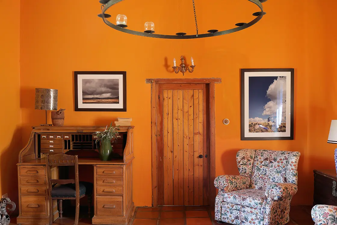 Perfect Hideaways real estate property: Indoor living space with orange walls and terracotta floors. An antique cabinet, vintage furniture, and wooden door. Zeekoegat Farm in Riversdale.