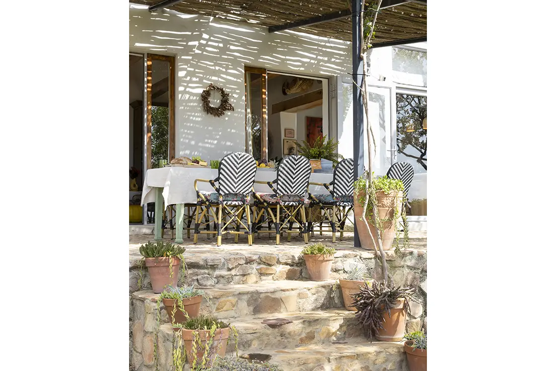 Perfect Hideaways real estate property: An outdoor dining area covered by a pergola, with black and white striped bistro chairs. Potted plants line stone steps from the garden. Barncroft in Napier.