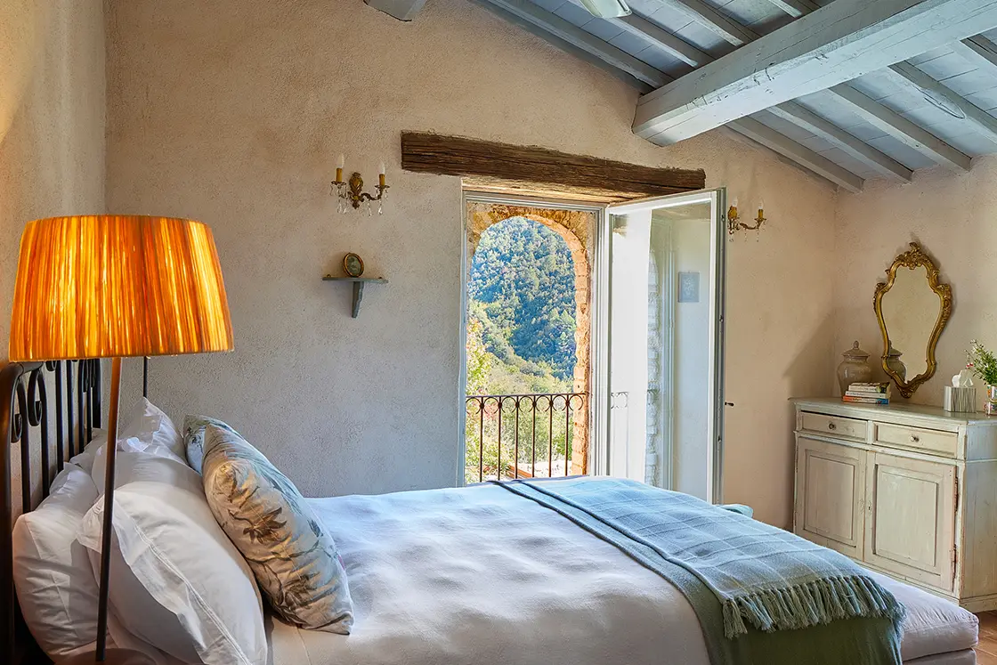 Perfect Hideaways real estate property: A bedroom in a restored 17th-century villa, which features a double bed and rustic decor, as well as an open doorway with a balcony alcove, and views of the Italian countryside. Casa Di Led in Spoleto.