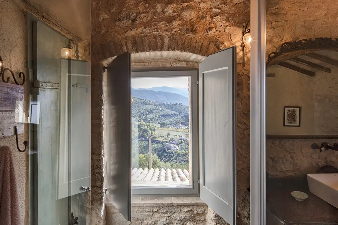 Perfect Hideaways real estate property: A natural stone bathroom interior with a decorative steel mirror and basin. An open window, showcasing views of Italy. Casa Di Led in Spoleto.