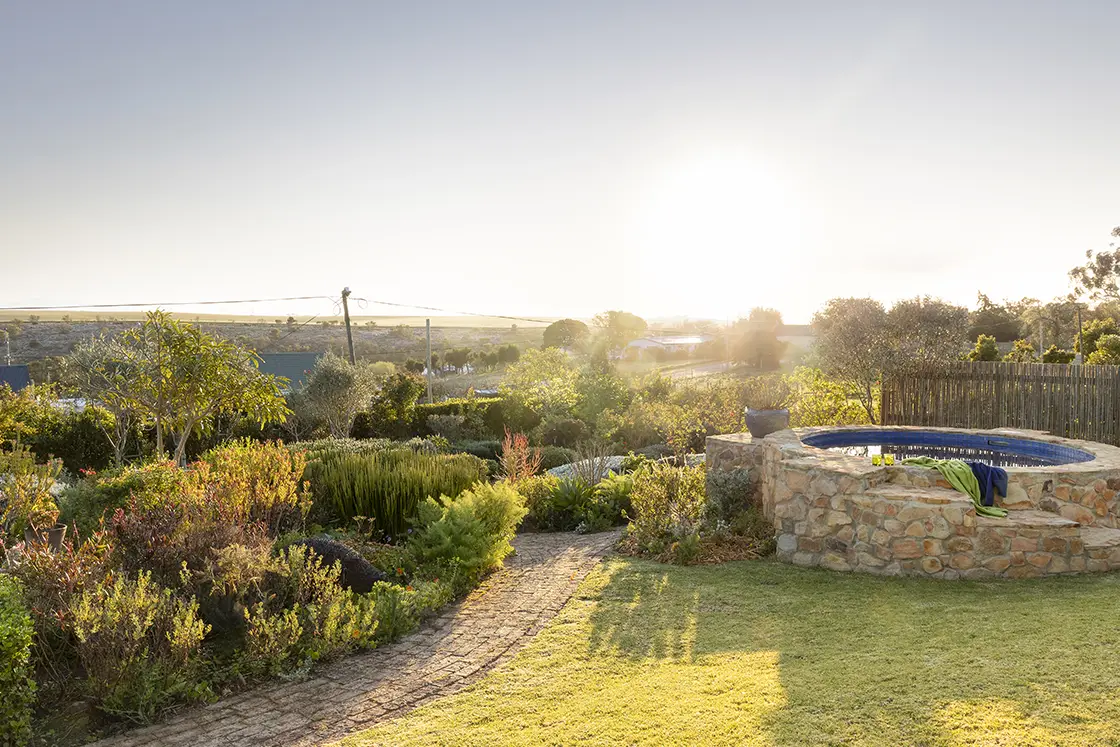 Perfect Hideaways real estate property: A garden path beside the circular swimming pool and meadow-style garden, with scenic views in the background. Barncroft in Napier.