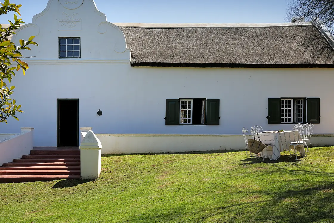 Perfect Hideaways real estate property: Table set for lunch in front of the historic national-monument house. Dark green shutters and thatch roof. Zeekoegat Farm in Riversdale.