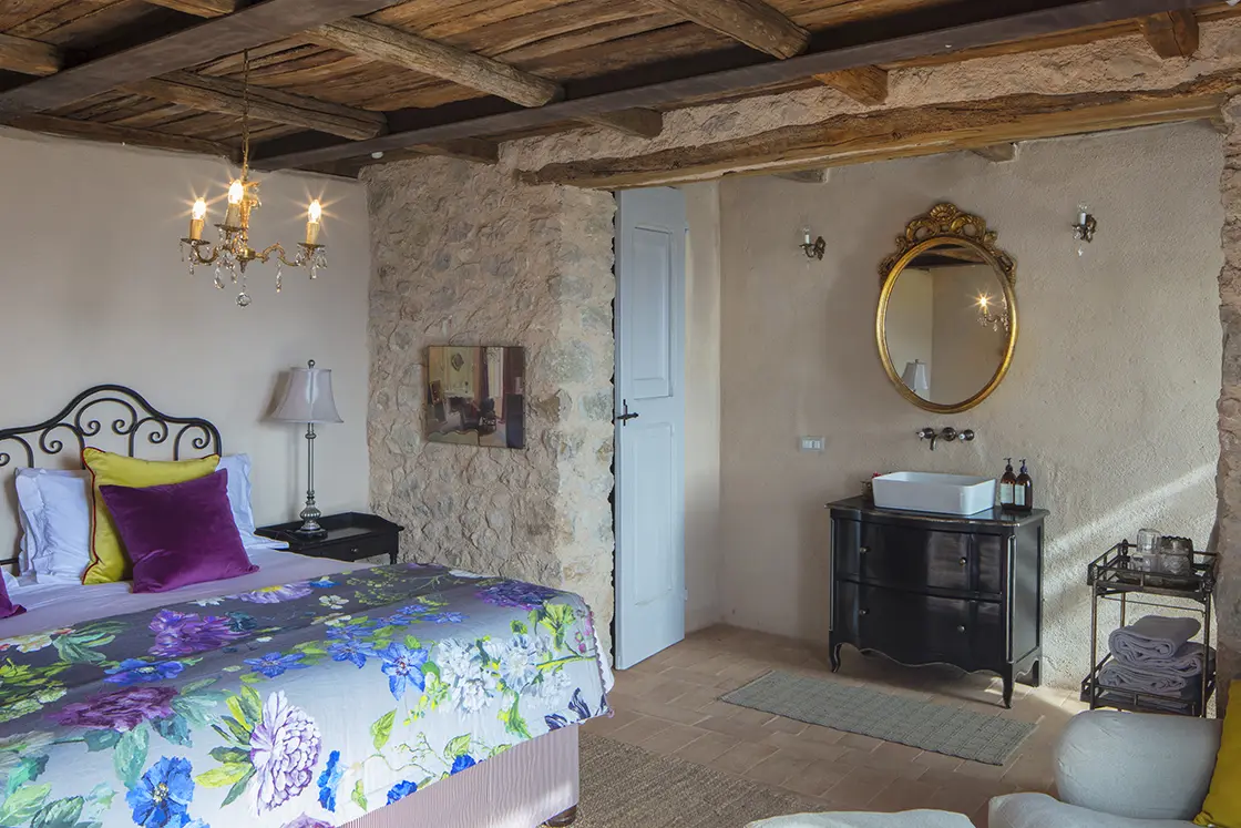 Perfect Hideaways real estate property: A bedroom with an en-suite bathroom, featuring a double bed with a floral throw and yellow accent color. Casa Di Led in Spoleto.