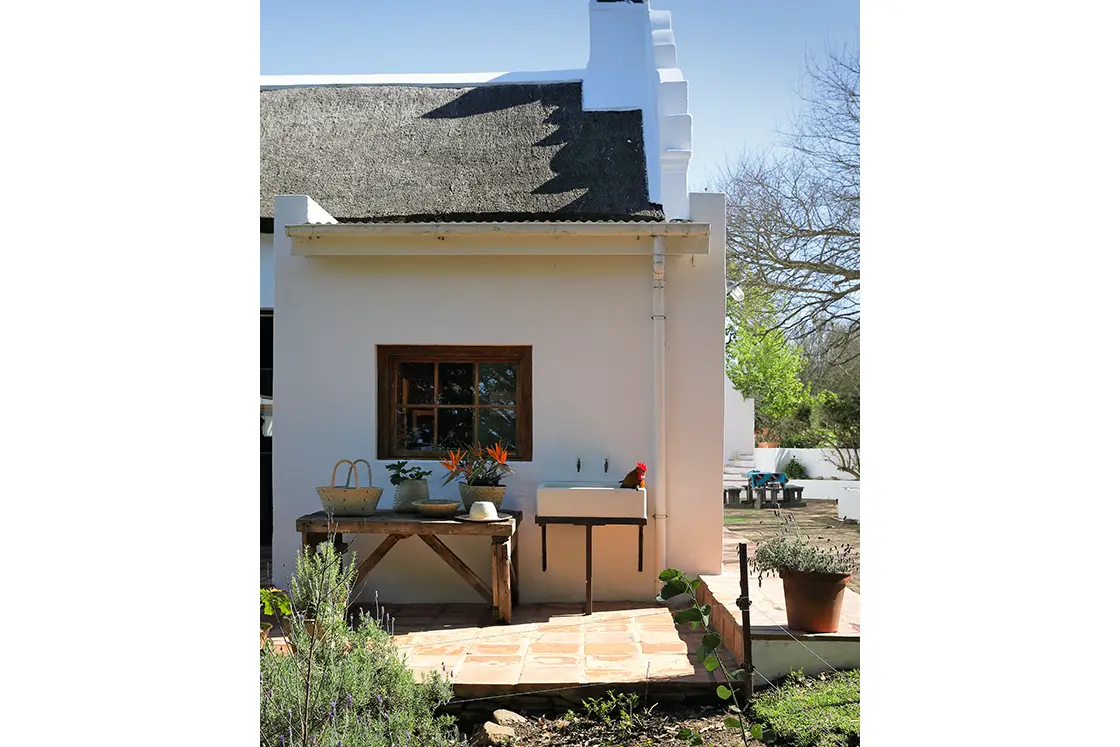 Perfect Hideaways real estate property: Outside wash station set on the patio of the farm-style homestead. Historic national-monument house with green door and windows. Steps lead to the second floor of the building. Grass in the foreground. Zeekoegat Farm in Riversdale.