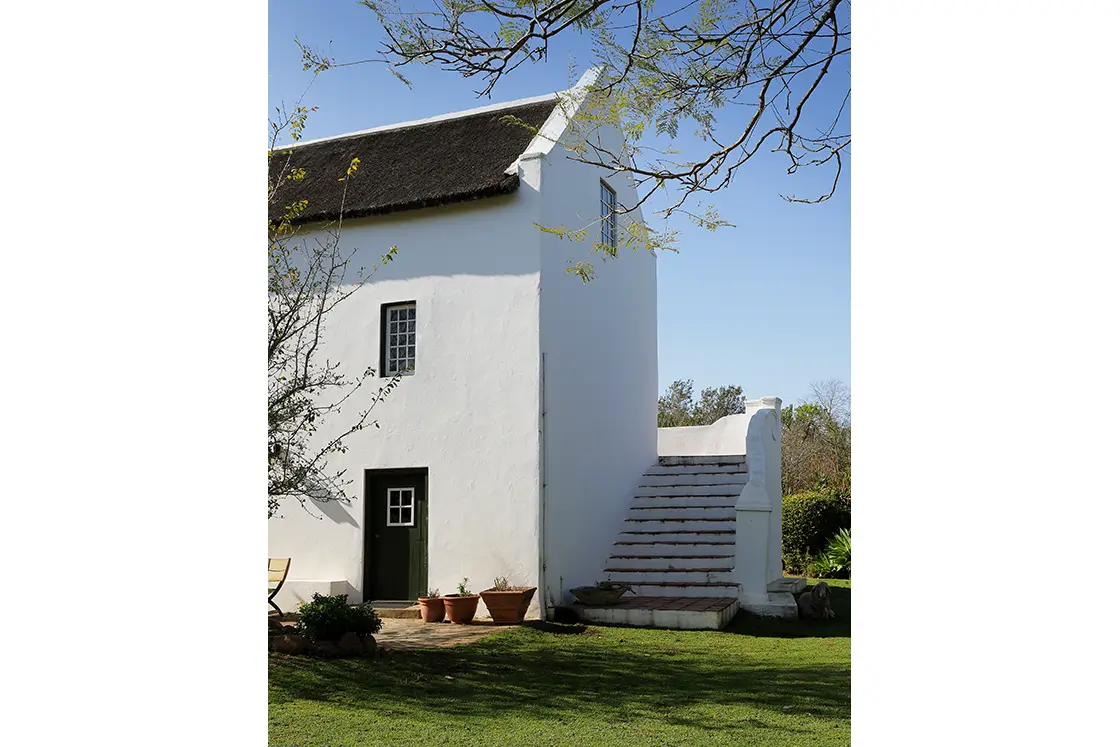 Perfect Hideaways real estate property: A two story building in the Cape Dutch style, featuring a set of wrap-around stairs leading to the second floor. The doors and windows feature a rich green accent colour. Zeekoegat Farm in Riversdale.