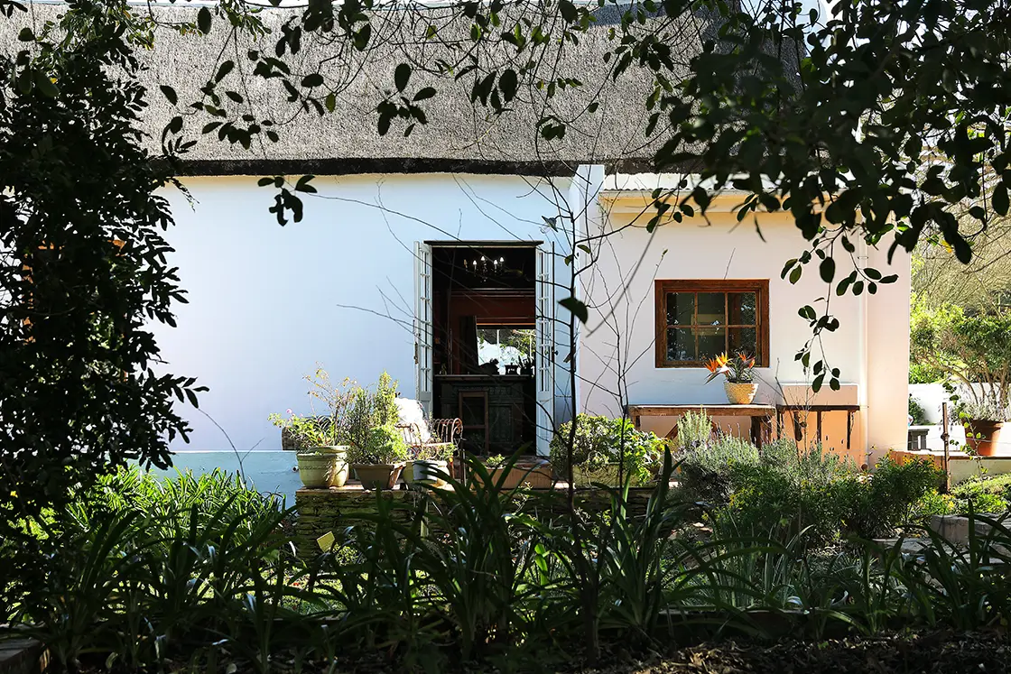 Perfect Hideaways real estate property: Shaded garden in front of the main house. A small outdoor patio and wash station, beside an open door. Zeekoegat Farm in Riversdale.