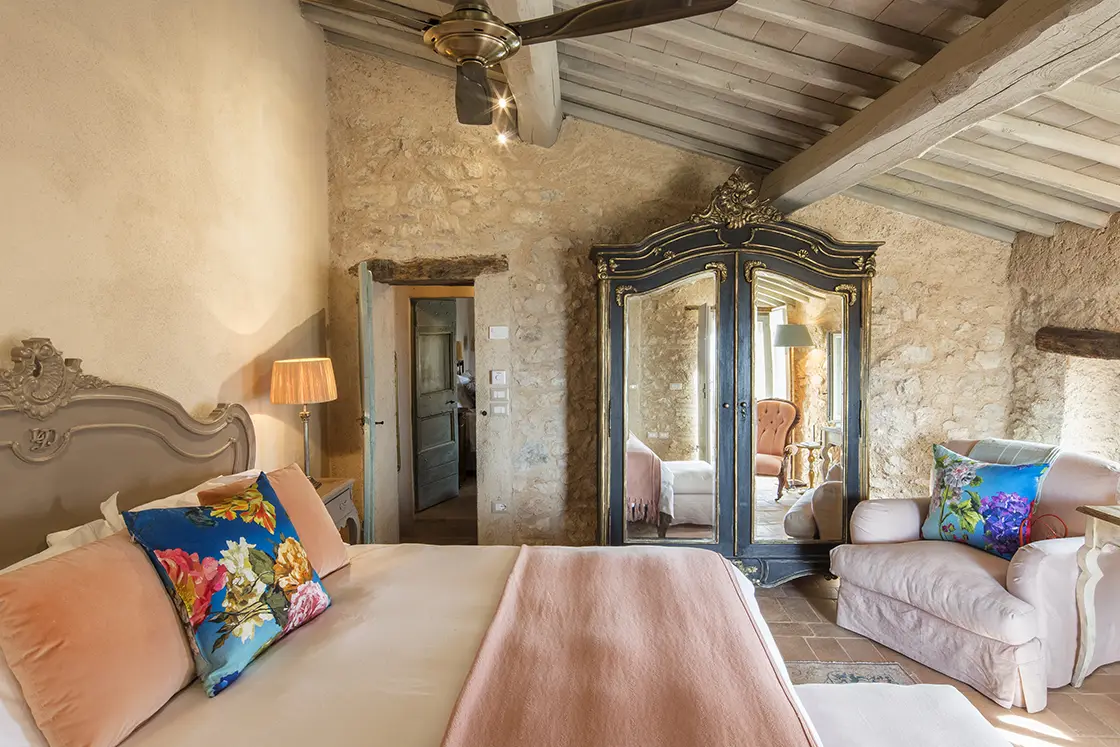 Perfect Hideaways real estate property: A bedroom with a double bed decorated by soft pink accent tones in the pillows and throw, beside an ornamental mirrored cabinet. Casa Di Led in Spoleto.