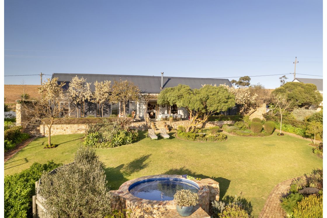 Select vegetation separates the grass lawn, highlighting a garden pool and open-view veranda. Overberg.