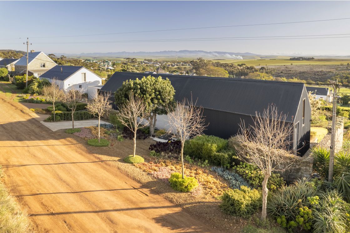 Wide angle view of contemporary barn style house in Napier, Overberg. Dirt road lined with trees.