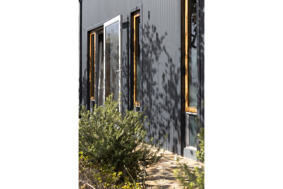 Sleek shuttered windows framed by corrugated walls. Open doorway and narrow pathway. Overberg.