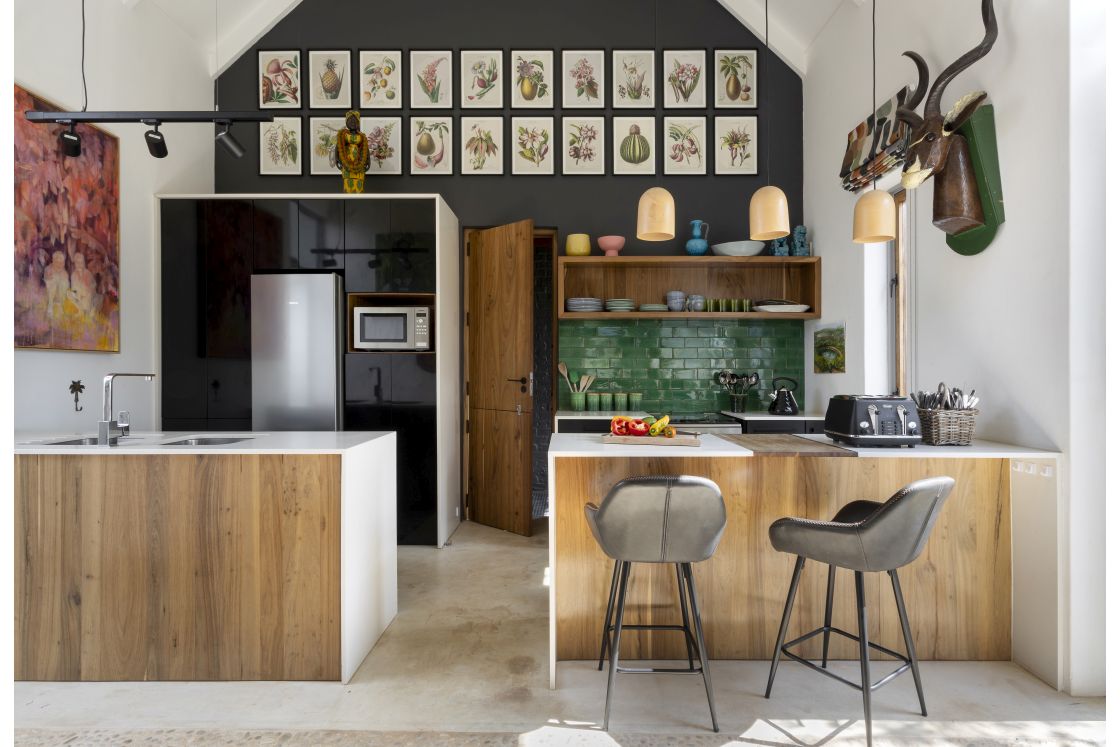 View of kitchen wash station, stove top, and counter space. Overhead storage, and fridge with scullery attached. Single wooden door. Overberg.