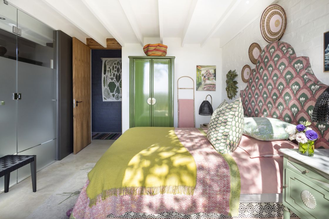 Large bedroom with decorative pink master bed and bedside table. Green cupboard space and frosted glass beside wooden door. Overberg.