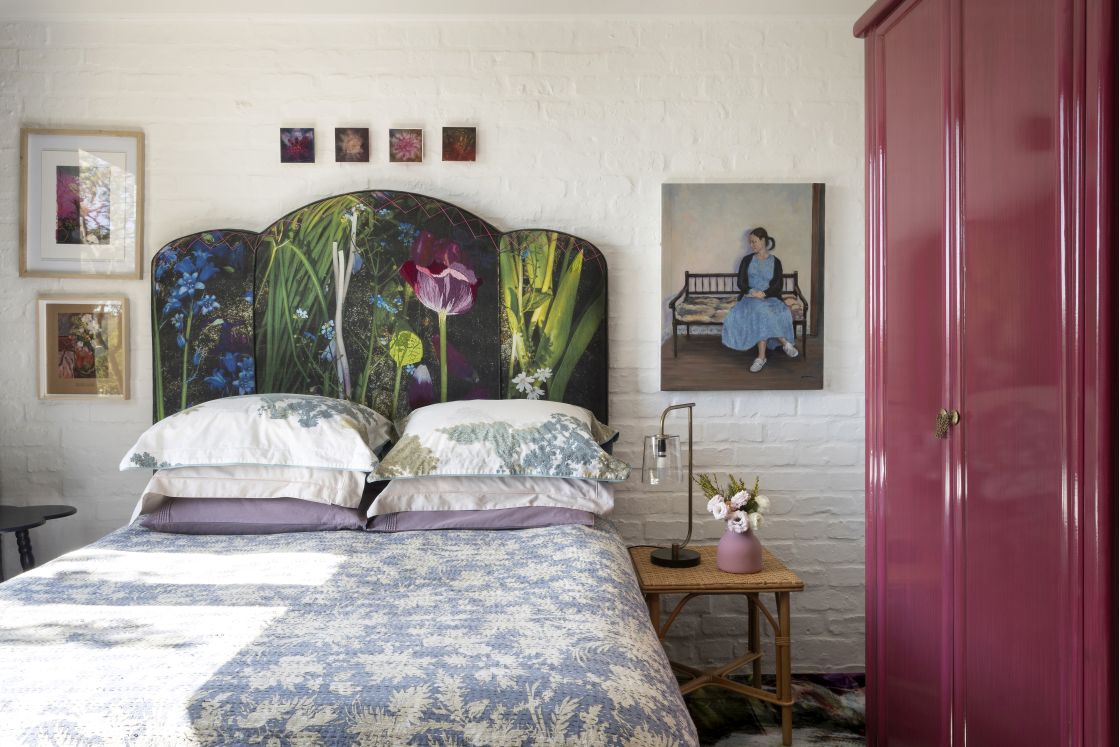 Blue patterned double bed , forest tapestry headboard against white brick wall. Full length purple cupboard. Overberg.