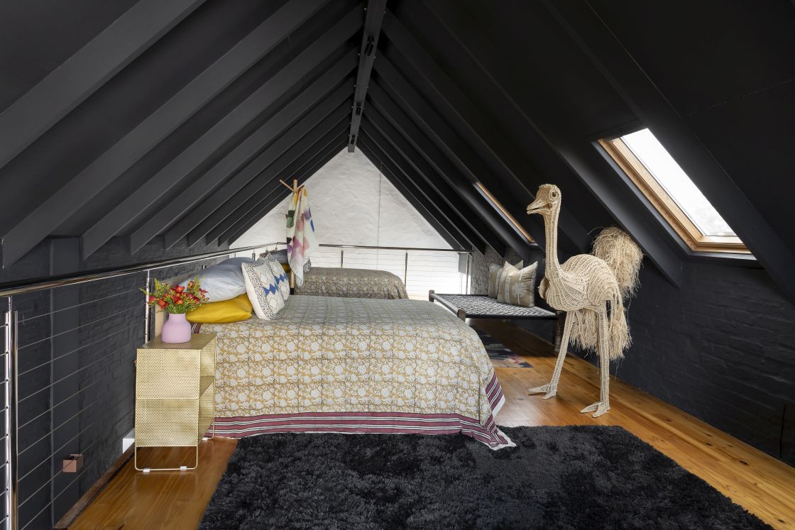 Attic loft space with two double beds and skylight. Black tuft rug, lounger, and beaded ostrich sculpture. Overberg.