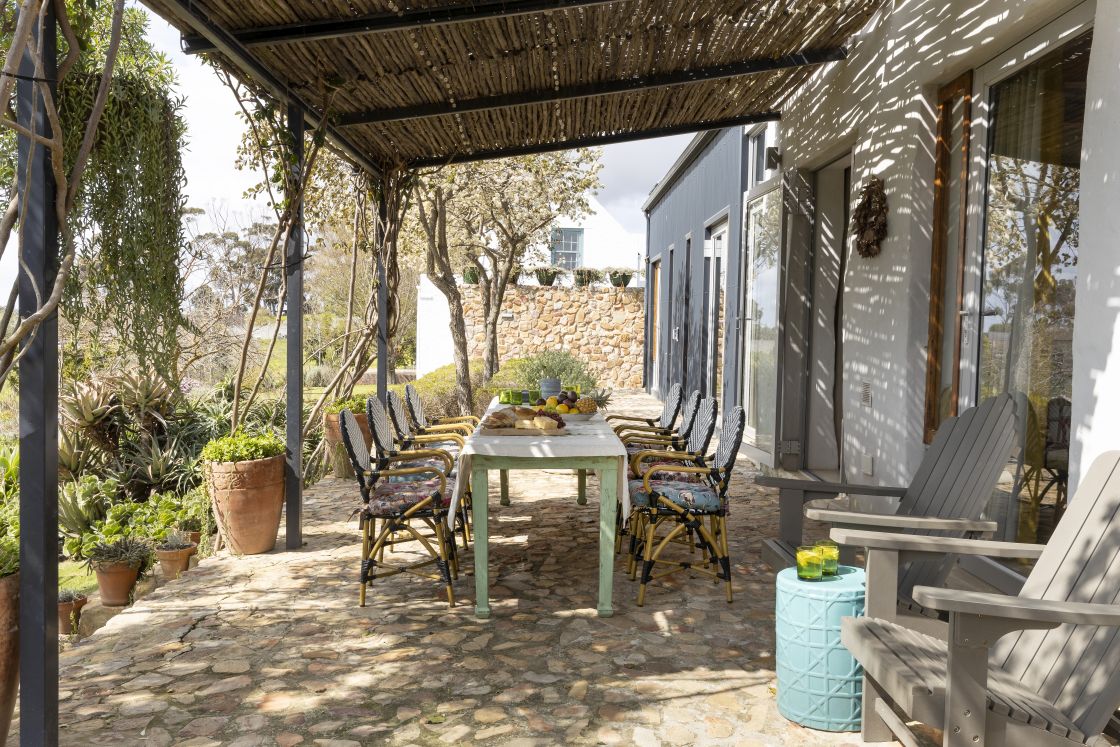 Veranda with stone floors, dining table, and 'Rietdak' ceiling. Potted vegetation decorates the outdoor area. Overberg.