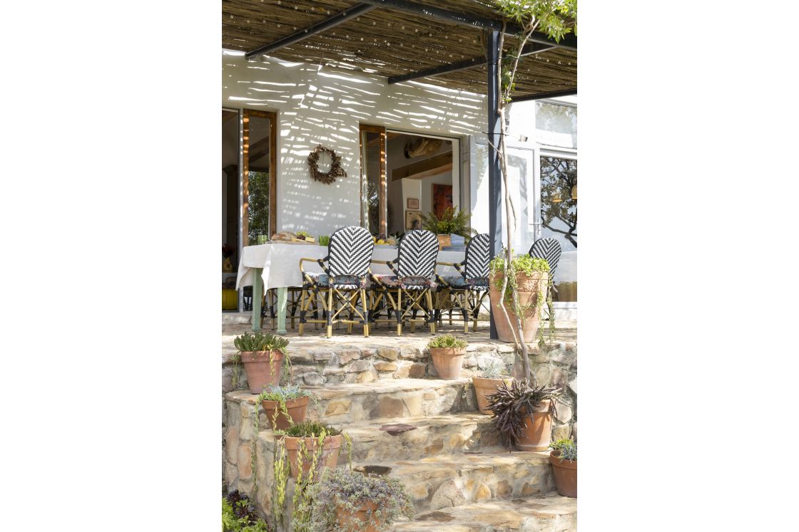 Pergola covered dining area with outdoor bistro chairs. Potted plants line stone steps from the garden. Overberg.