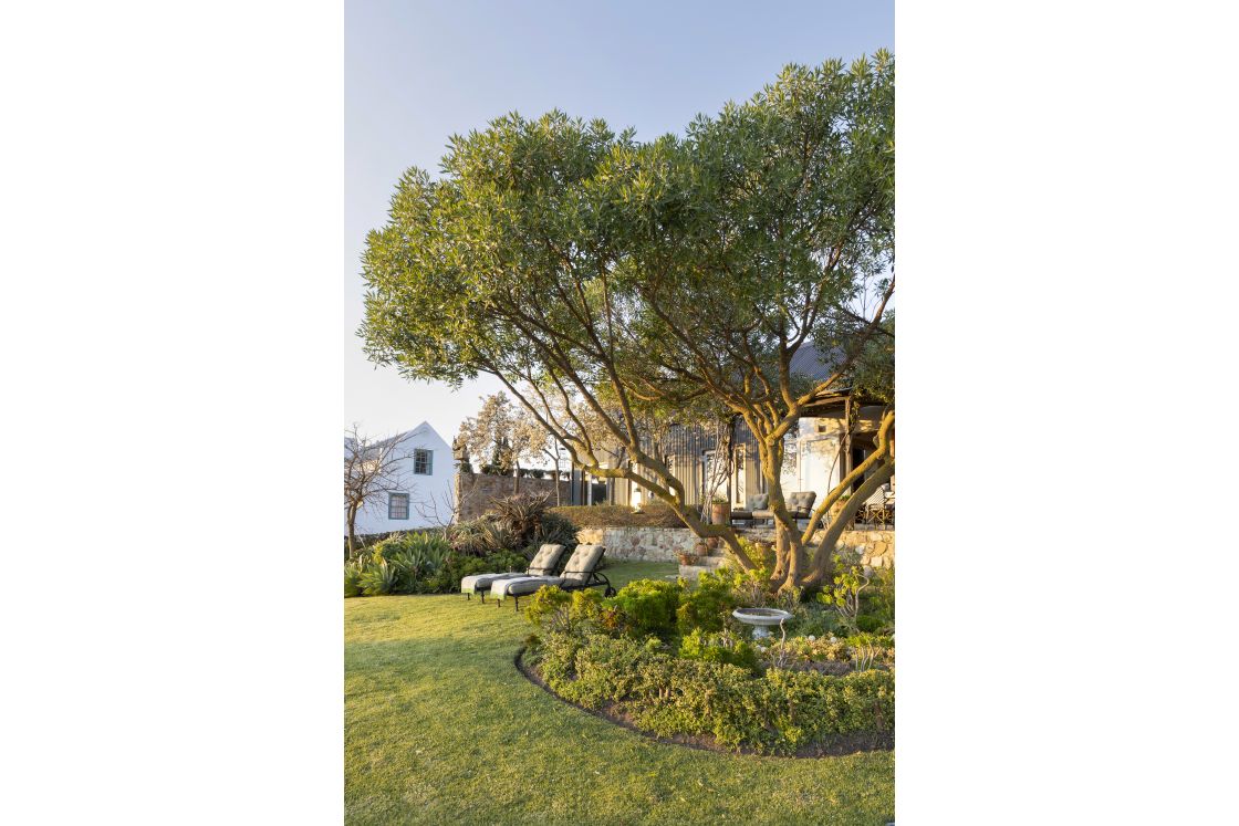 Garden area with outdoor seating, bird bath, and contemporary barn style home in backdrop. Overberg.