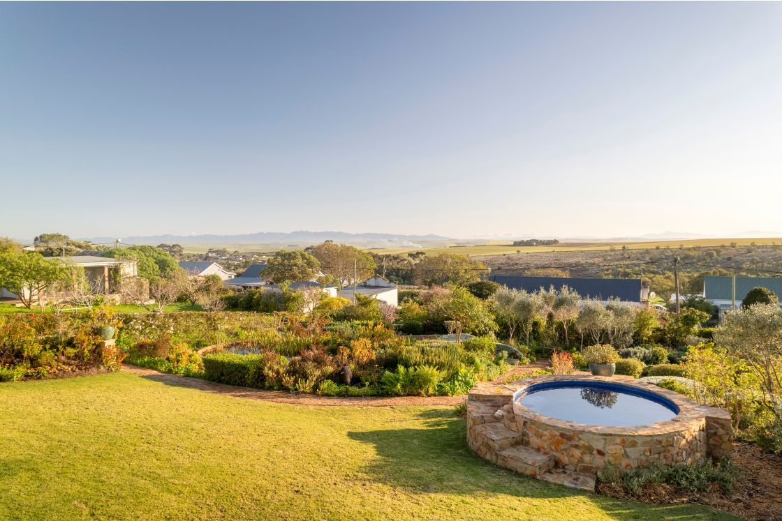 Meadow garden with fishpond and natural stone steps into circular swimming pool. Overberg.