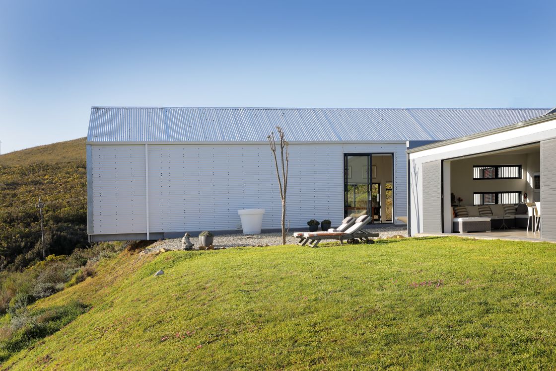 A minimalist white house located on a hillside, surrounded by greenery and offering a scenic view of the landscape.