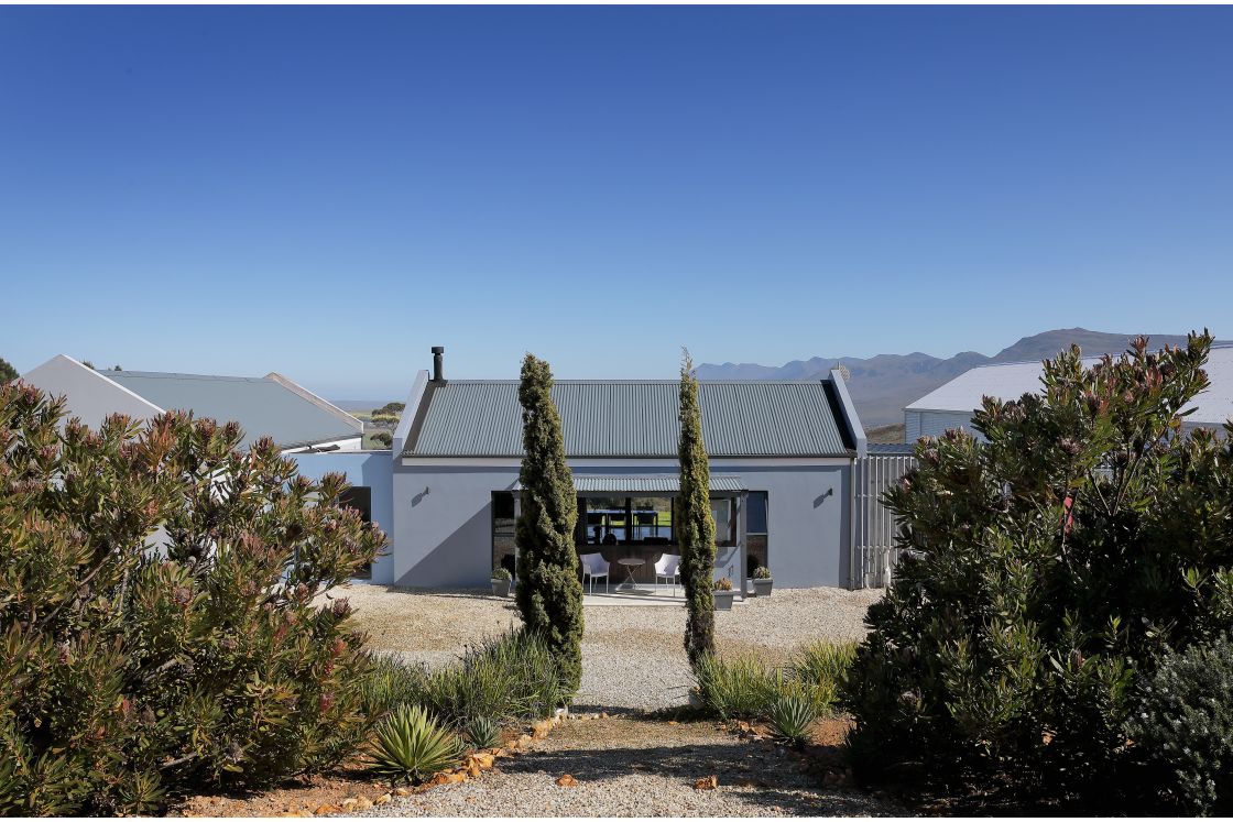 A house featuring a corregated roof and a paved driveway, set against a clear sky backdrop.