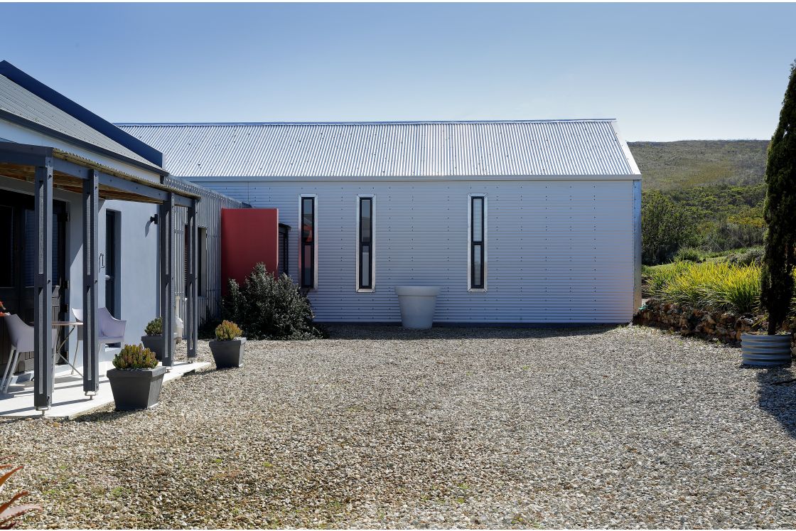 A corregated iron white house adorned with a bold red door and a lovely patio, perfect for outdoor furniture.