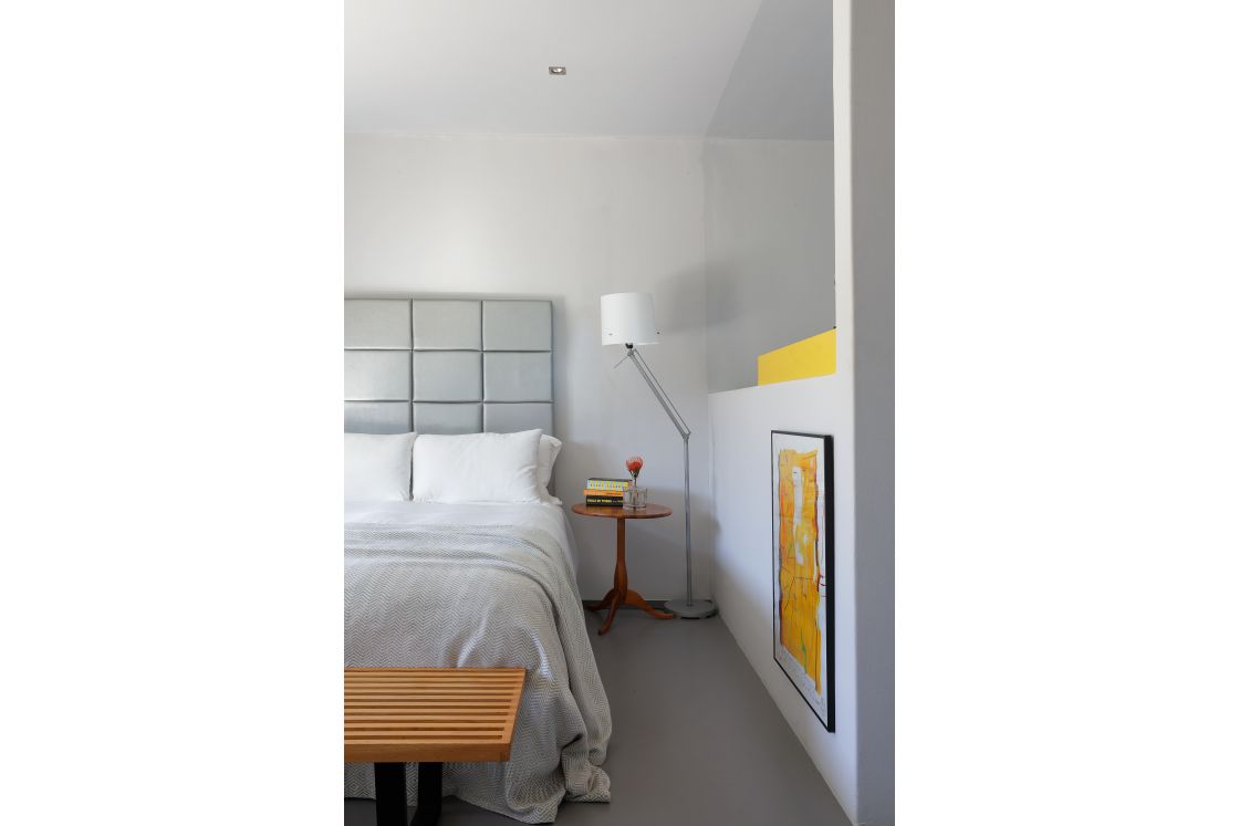 A well-decorated bedroom displaying a bed, a lamp, and yellow paintings.