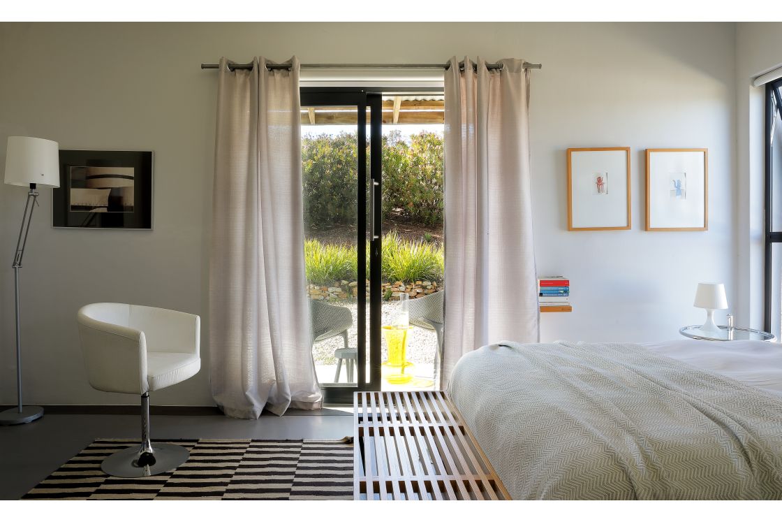 A cozy bedroom featuring a bed, a chair, and a sliding glass door that opens to a serene outdoor view.