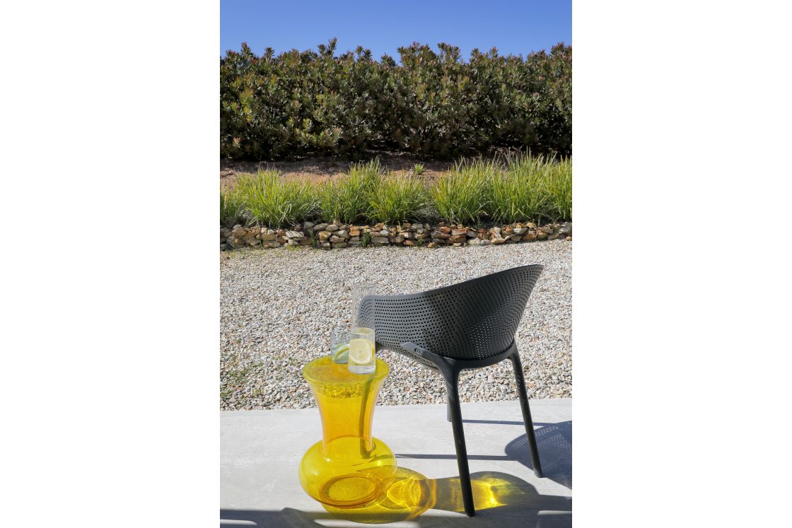 A grey chair beside a refreshing glass of lemonade on a sunny patio overlooking the garden.