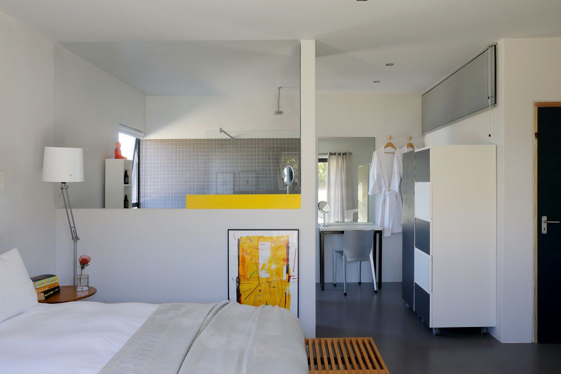 A white bed in a room with yellow painting and modern decor, en-suite bathroom.