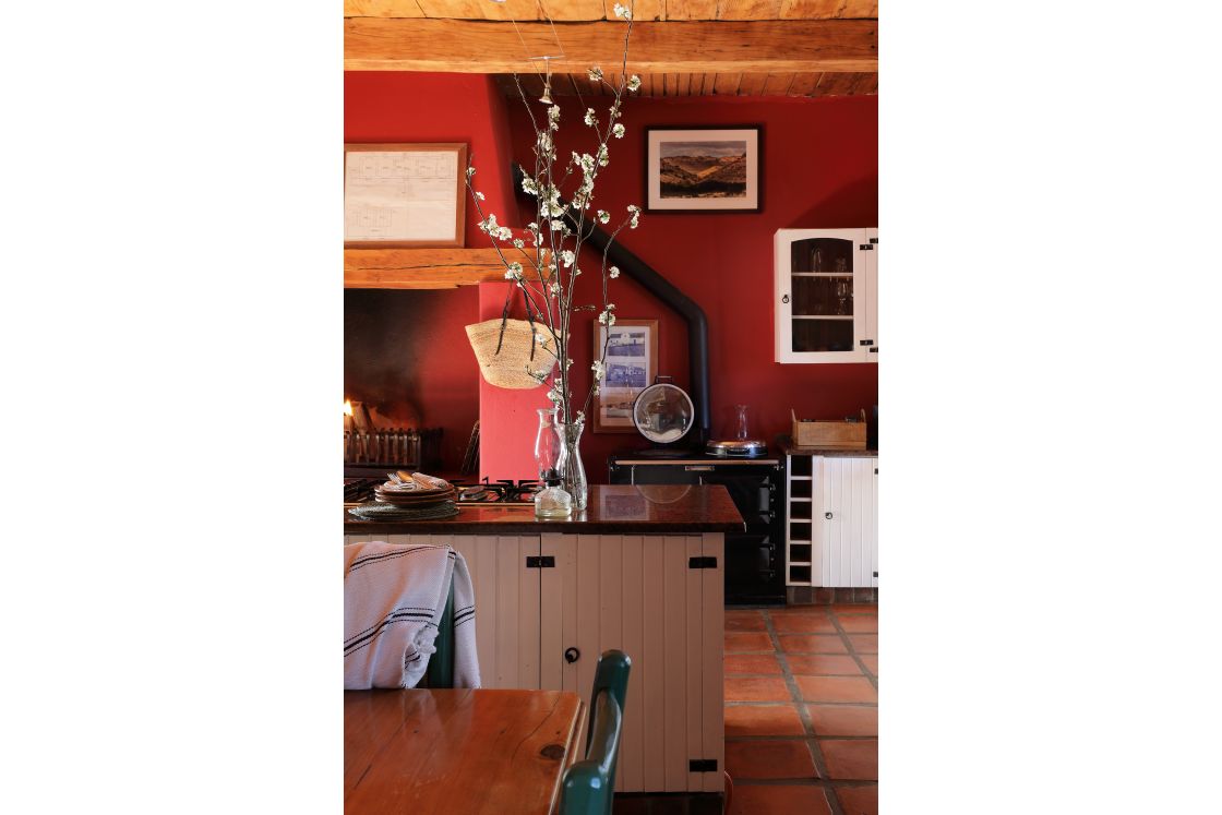 Central kitchen island featuring black stone countertop, with built-in gas stove top . Against the back wall is an additional stove and indoor fireplace.