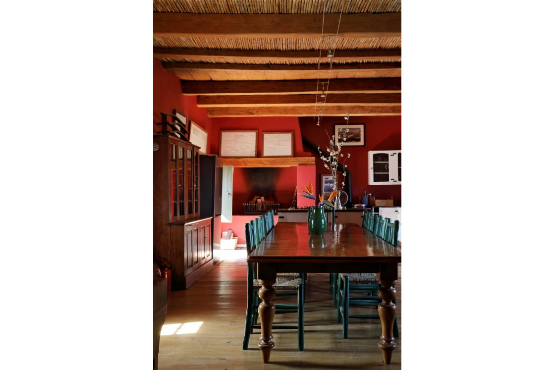 Dining room within the main house featuring red walls, wooden floors, and dining table surrounded by blue chairs.